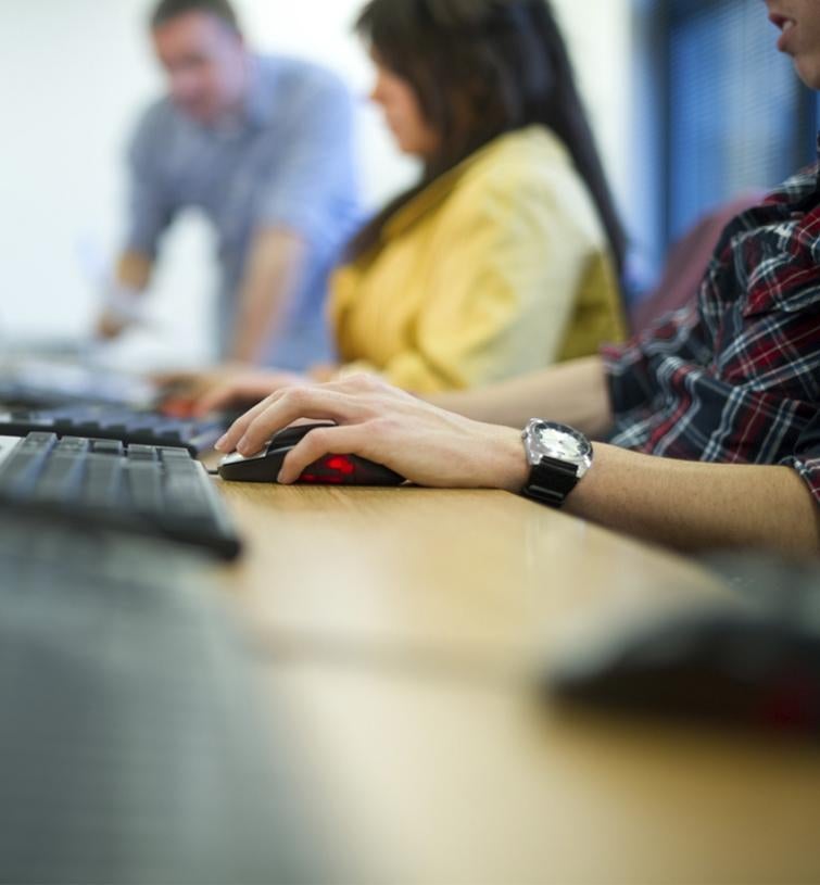 Three people sit at a long table and work on computers. 