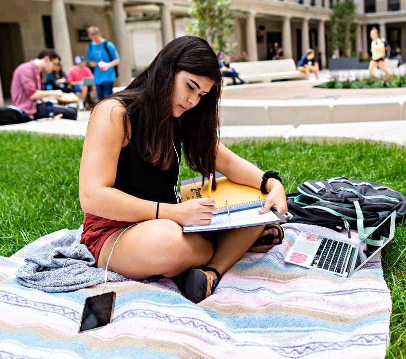 A student writes in a notebook on the campus lawn.